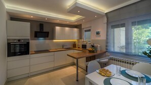 A modern kitchen with white cabinets, a built-in oven, and a dining area with a table set for two. - Beautiful Villa Suton with a Private Pool (Pula)
