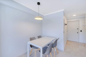 A modern dining area with a white table and grey chairs, a hanging pendant light, and a white door in the background. - Alto Vitacura I - Stunning City Views (Las Condes)