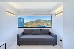 A modern room with a grey sofa, a large window with a city view, and recessed lighting. - Alto Vitacura I - Stunning City Views (Las Condes)