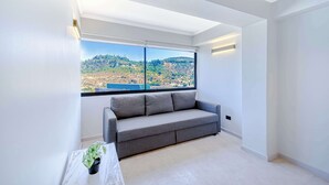 Una sala de estar moderna con un sofá gris, una mesita con una planta y un amplio ventanal con vistas panorámicas.
