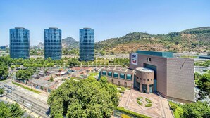 A cityscape with modern buildings, a parking lot, and a landscaped area with trees.