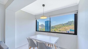 A modern room with a white table and chairs, a large window with a city view, and a pendant light.