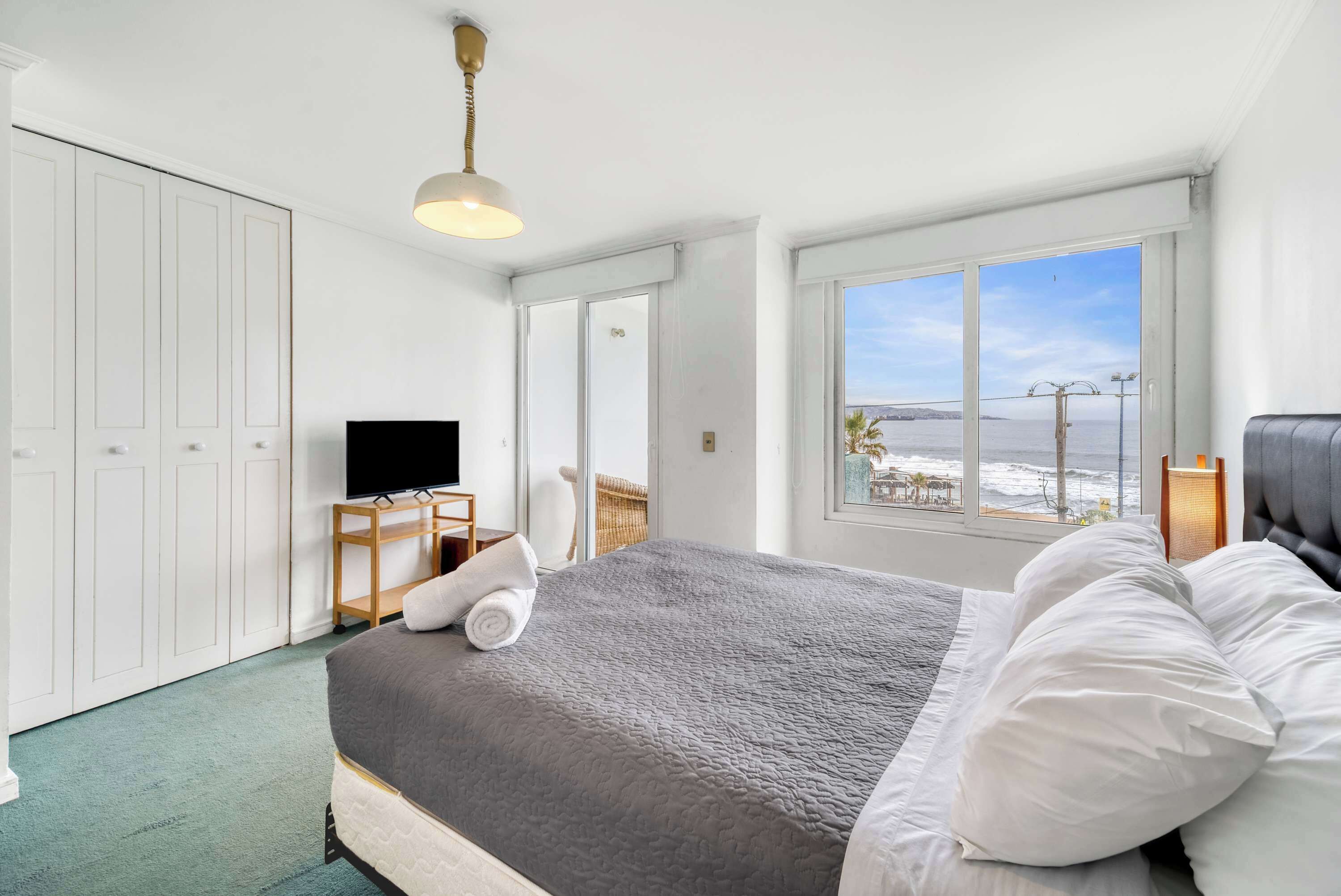 Une chambre à coucher avec un lit, une télévision, un bureau et une fenêtre donnant sur la mer.