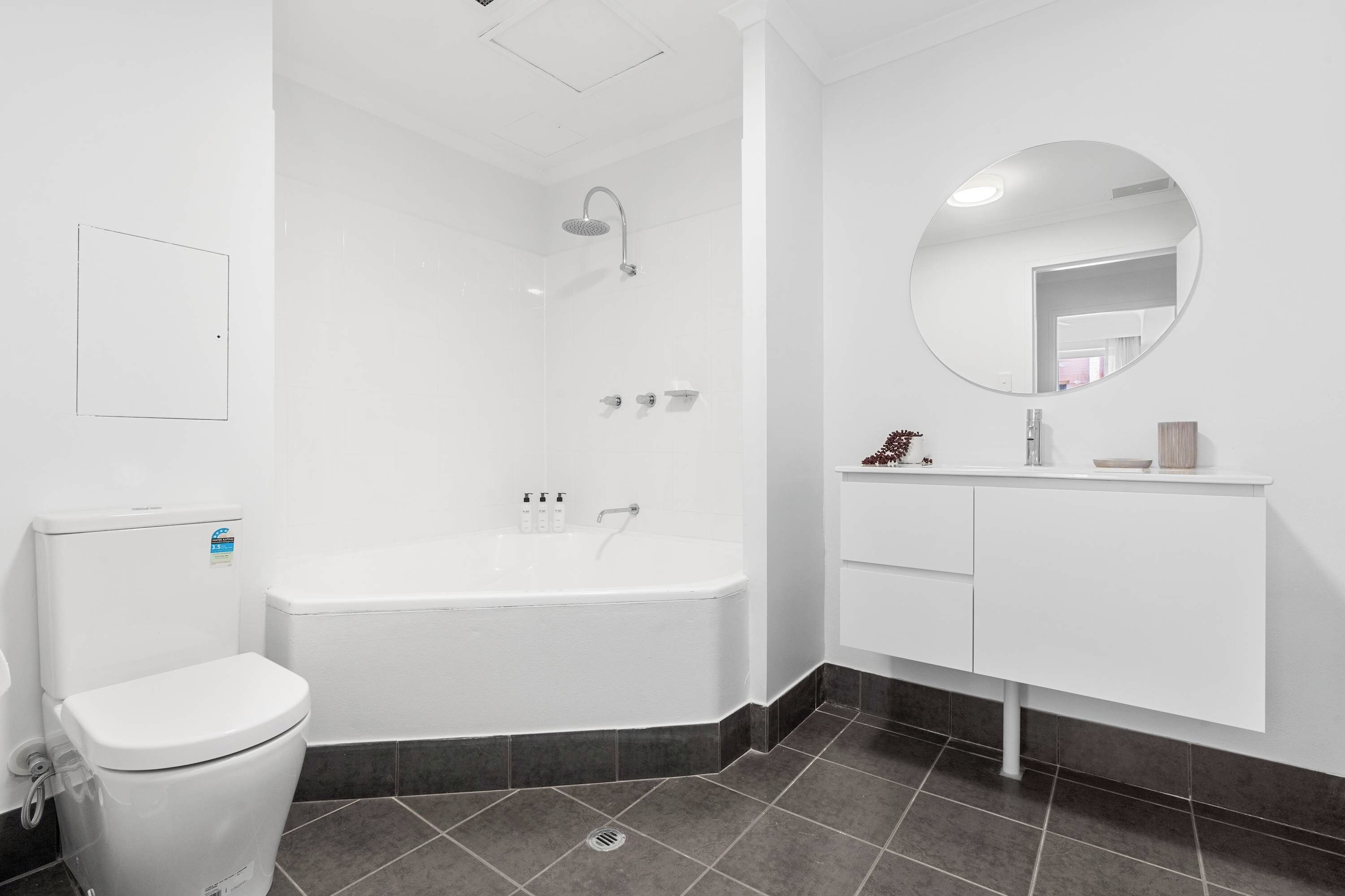 A modern bathroom with a white toilet, a bathtub, a shower, and a vanity with a mirror.