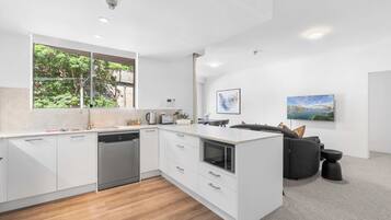 A modern kitchen with white cabinetry, a dishwasher, and a large window overlooking greenery.