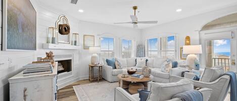 A spacious living room with a white color scheme, a ceiling fan, and large windows.