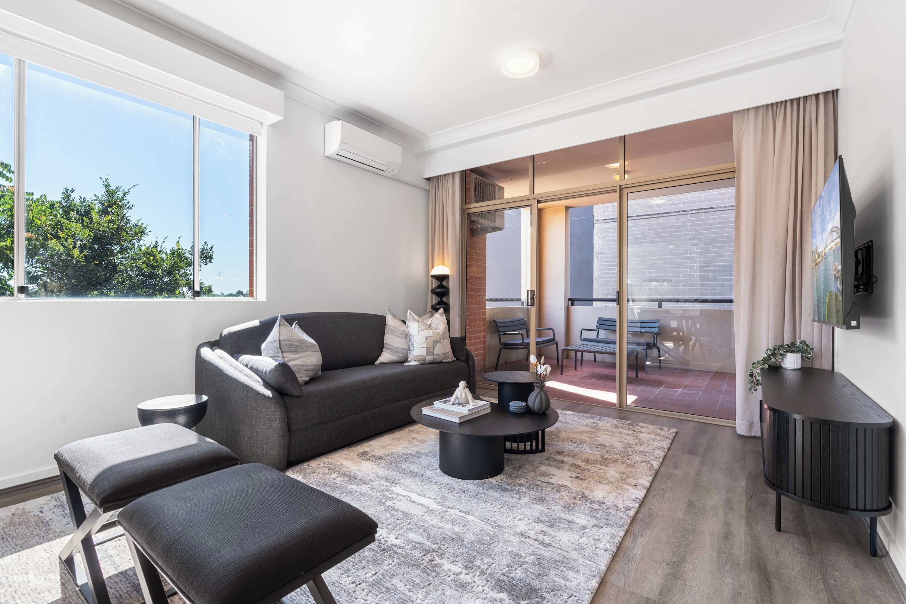 A modern living room with a grey sofa, black ottomans, a coffee table, and a TV on a black stand.