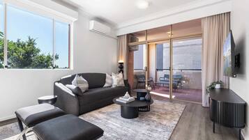 A modern living room with a grey sofa, black ottomans, a coffee table, and a TV on a black stand.