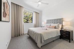 A neatly arranged bedroom with a large bed, a bedside table with a lamp, and a window with curtains. - Camperdown Cozy Corner 3 (Camperdown)
