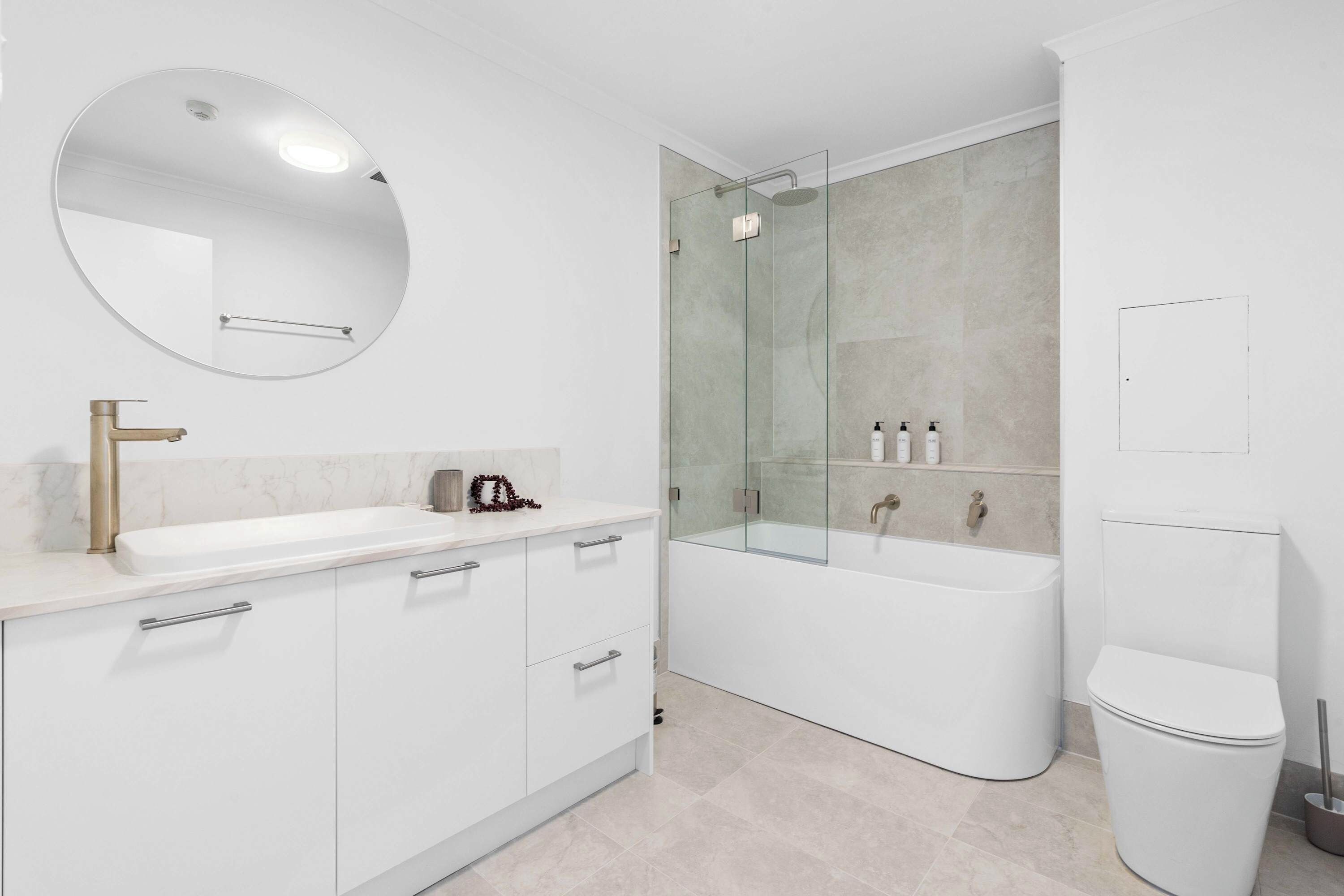 A modern bathroom with a white sink, a round mirror, a glass-enclosed shower, and a white toilet.