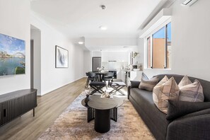 A modern living room with a dark sofa, a round coffee table, and a dining area with a black table and chairs. - Camperdown Cozy Corner 3 (Camperdown)