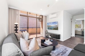 A modern living room with a grey sofa, a coffee table, and a large window overlooking a cityscape. - Camperdown Cozy Corner 6 (Camperdown)