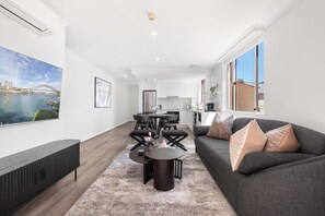 Relax in a spacious living area with a comfortable sofa and dining table, opening to a well-equipped kitchen with large windows offering views of the surrounding area.