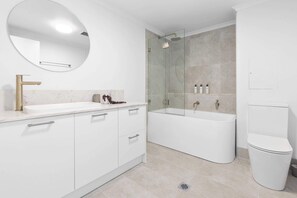 Modern bathroom with a large oval mirror, gold faucet, walk-in shower, handheld showerhead, bathtub, and white toilet.