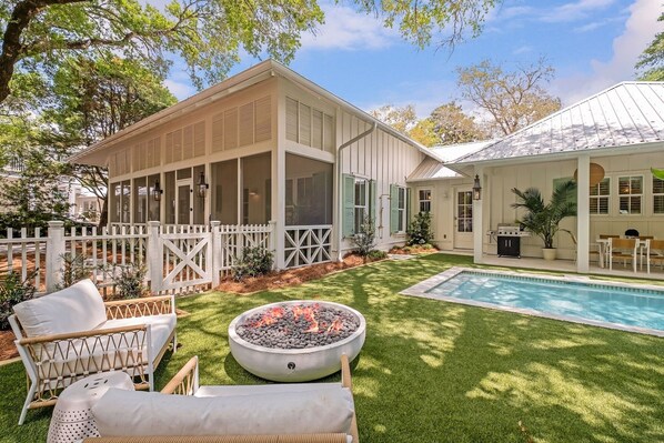 A backyard with a pool, a fire pit, outdoor furniture, and a covered patio area.