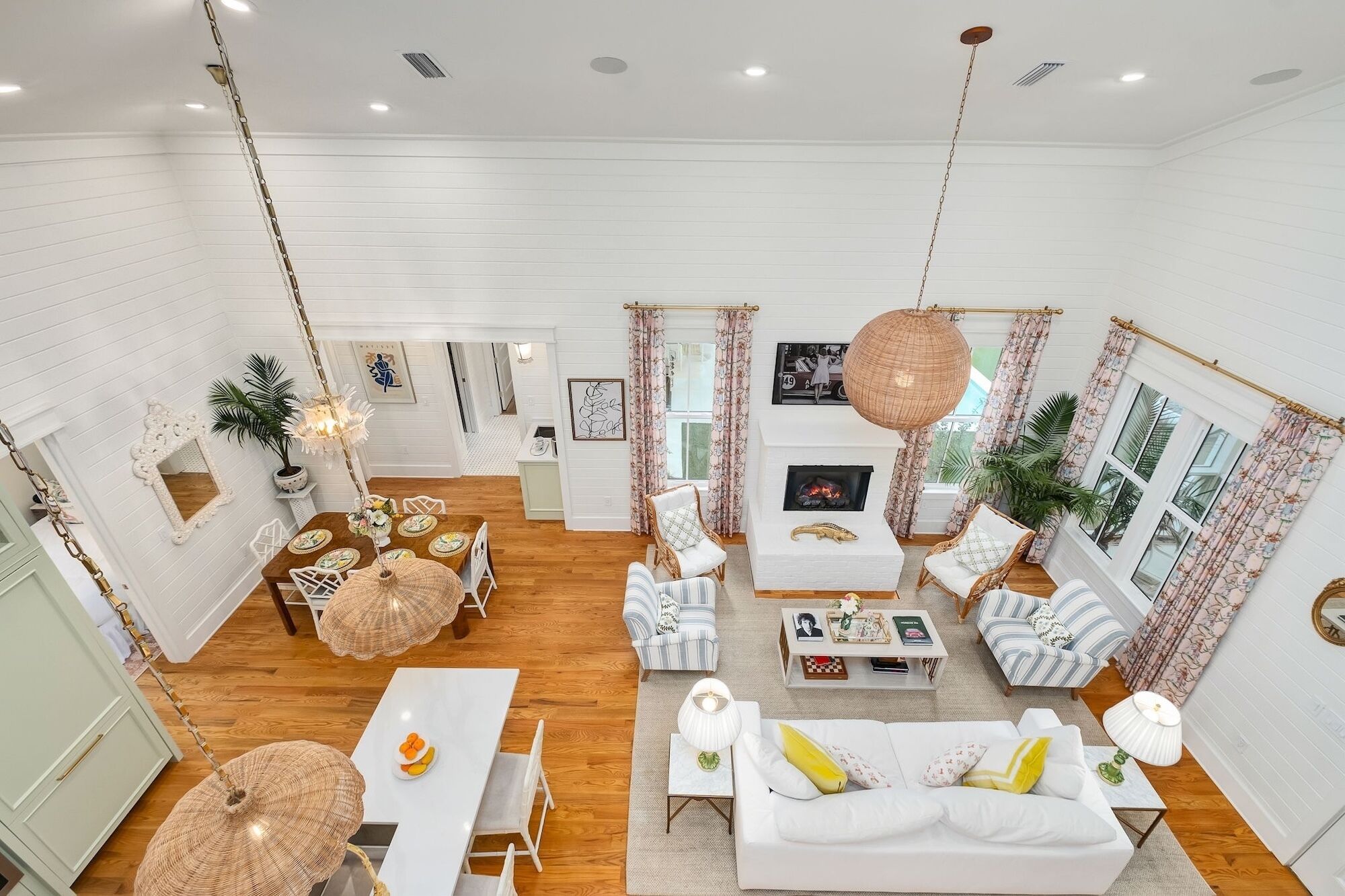 A spacious living room with a white sofa, striped armchairs, a dining area with a white table, and a fireplace.
