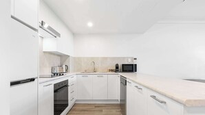 A modern kitchen with white cabinetry, a wooden floor, and a marble countertop. - Camperdown Cozy Corner 8 (Camperdown)