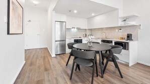 A modern kitchen with white cabinetry, a stainless steel refrigerator, and a dining area with a round table and grey chairs. - Camperdown Cozy Corner 9 (Camperdown)