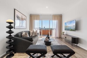 A modern living room with a sofa, two ottomans, a coffee table, and a TV mounted on the wall.