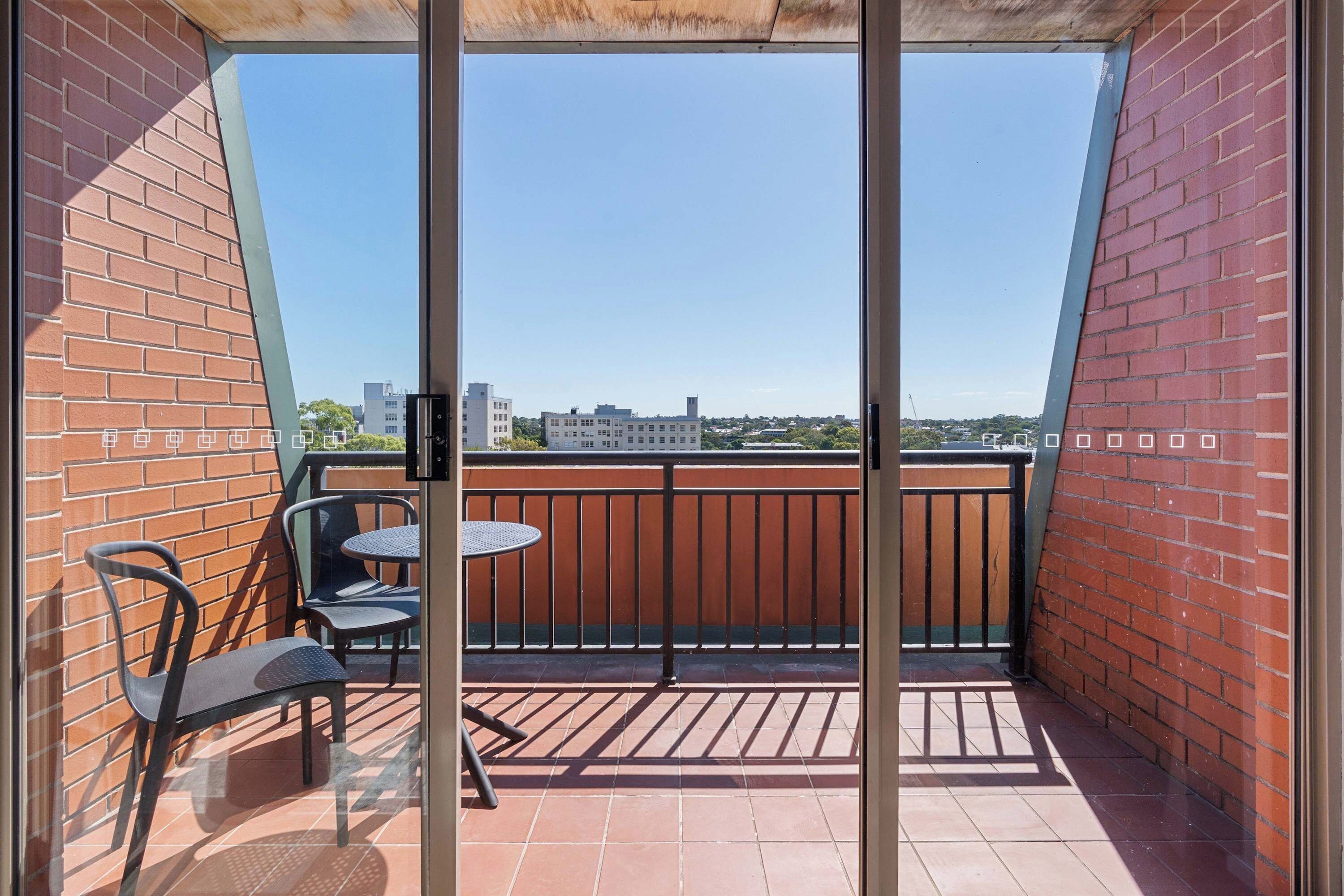 A balcony with a view of buildings, a table, and two chairs.