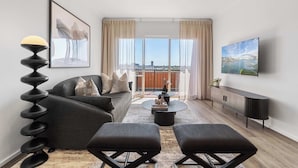 A modern living room with a sofa, two ottomans, a coffee table, and a TV mounted on the wall.