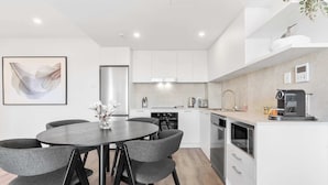 A modern kitchen with white cabinets, a central island, and a dining area with a round table and chairs.
