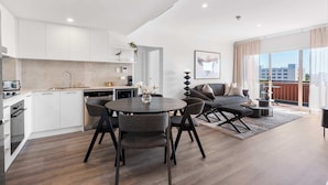 A modern kitchen with white cabinets, a dining area with a round table and chairs, and a living area with a sofa and a coffee table.