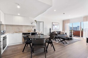 A modern kitchen with white cabinets, a dining area with a round table and chairs, and a living area with a sofa and a coffee table.