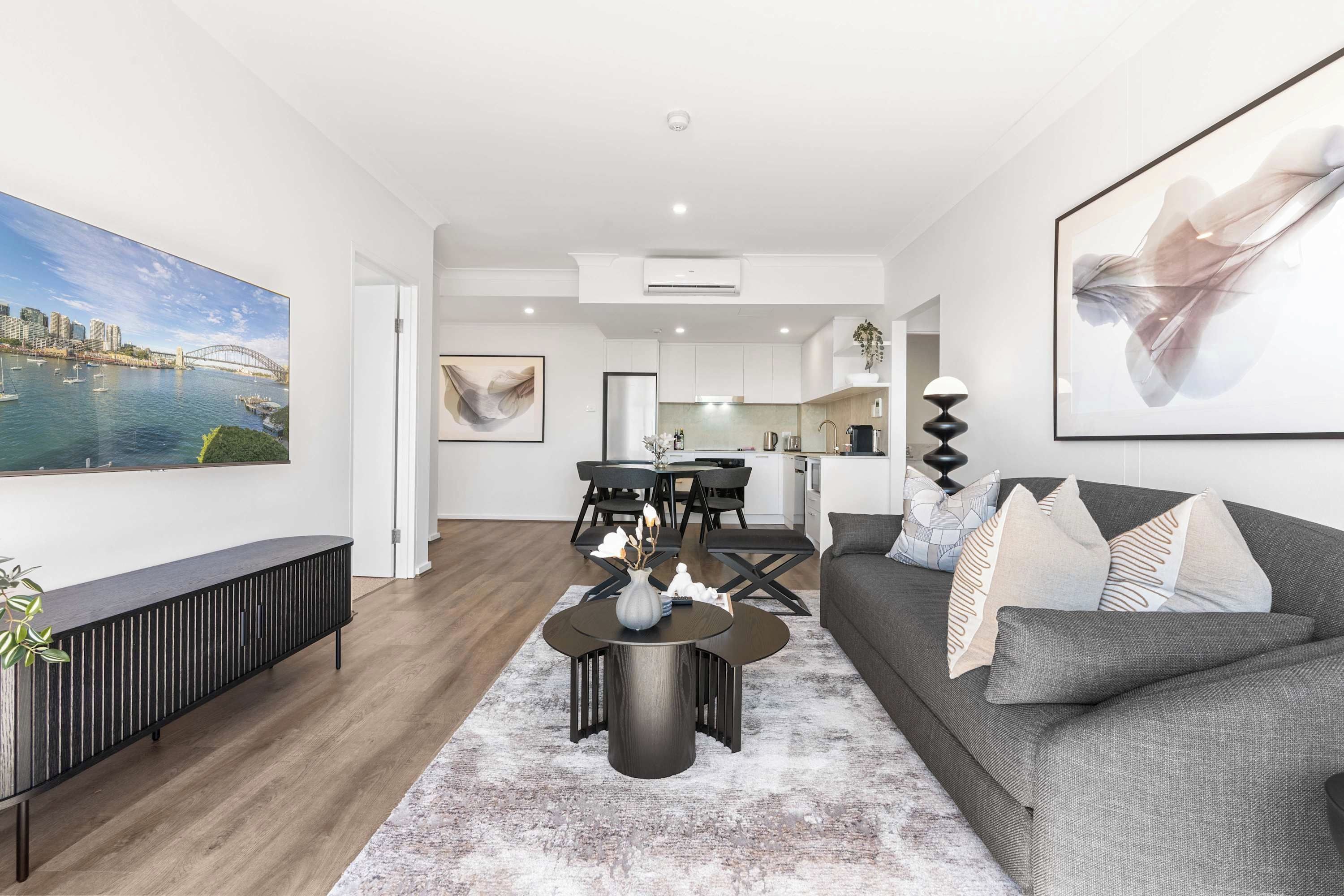 A modern living room with a grey sofa, a coffee table, and a dining area with a black table and chairs.