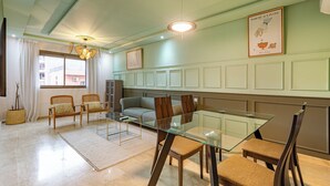 A modern dining area with a glass table and chairs, a sofa, and a large window with curtains. - Appartement de luxe au centre de Gueliz  (Marrakech)