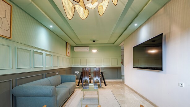 A modern living room with a sectional sofa, a dining table with chairs, a flat-screen TV mounted on the wall, and a ceiling light fixture. - Appartement de luxe au centre de Gueliz  (Marrakech)