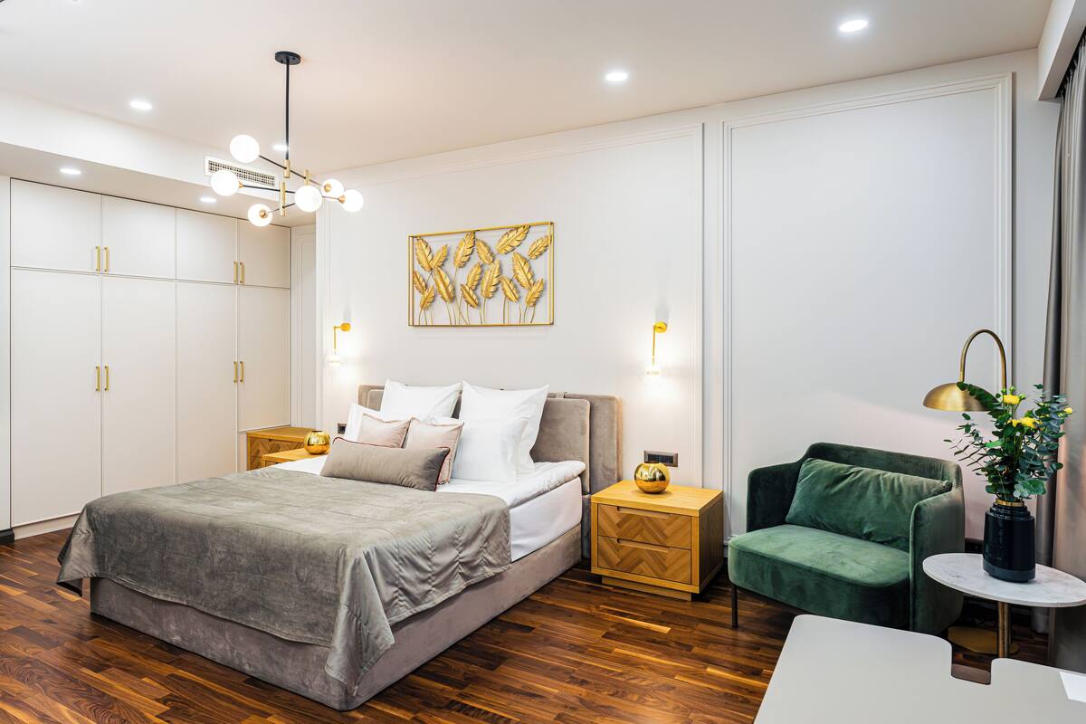 Ein modernes Schlafzimmer mit Bett, Nachttischen, einem grünen Sessel und einem Wanddekor.