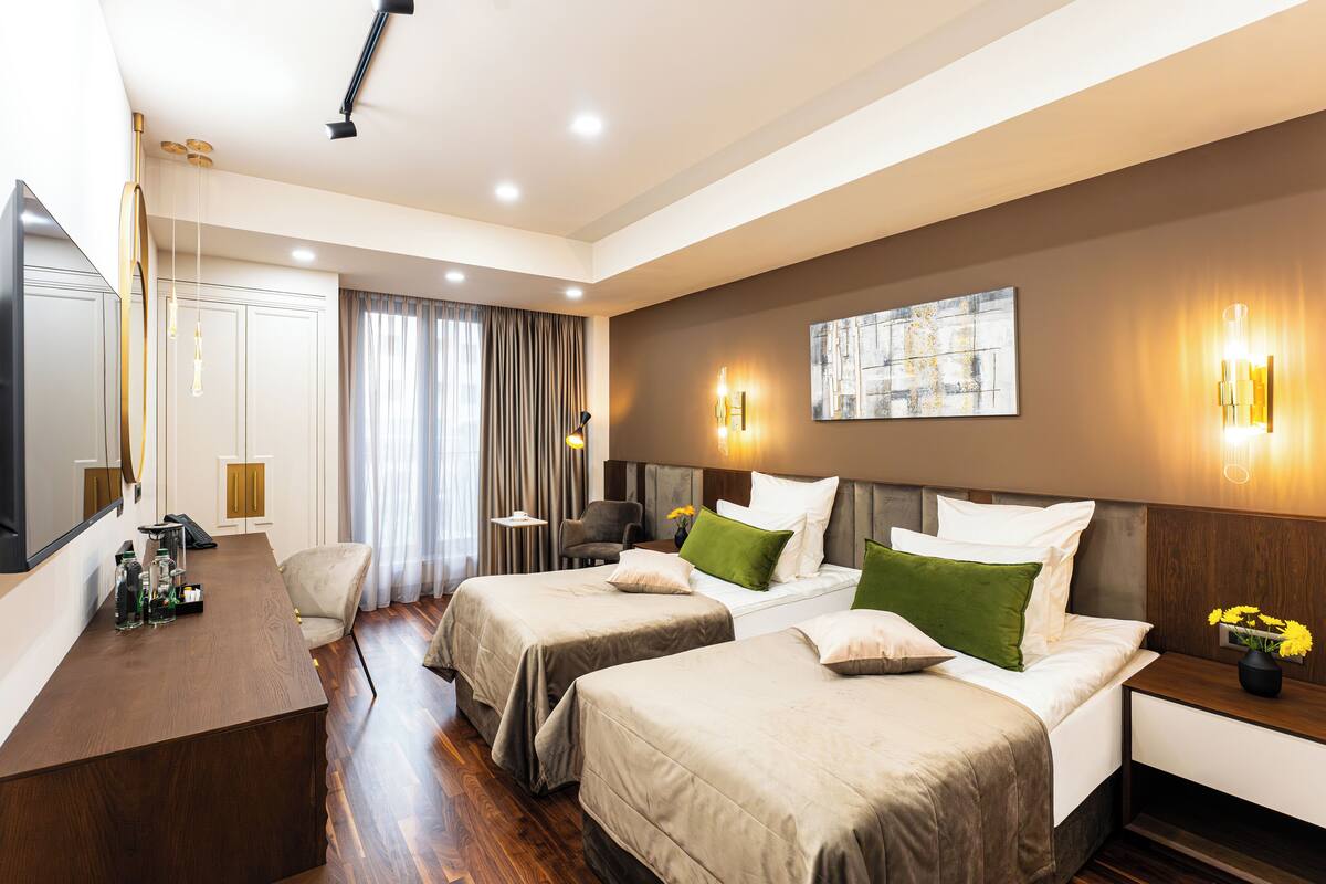 Ein Hotelzimmer mit zwei Betten, einem Schreibtisch und einem Stuhl. An der Wand hängt ein Gemälde und auf dem Nachttisch steht eine Vase mit Blumen.