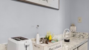 A kitchen with a toaster, a coffee maker, and a sign that says "Coffee Bar". - The Serenity at Peck Plaza (Daytona Beach)