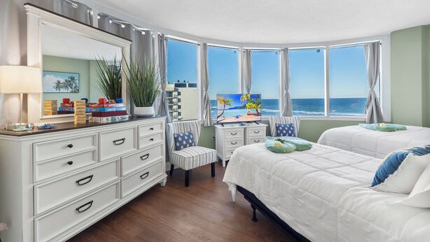 A bedroom with a large mirror, two beds, a dresser, and a view of the ocean. - The Serenity at Peck Plaza (Daytona Beach)