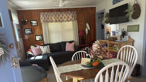Un salon chaleureux avec un plancher en bois, une table à manger avec des chaises, un canapé et un téléviseur fixé au mur.