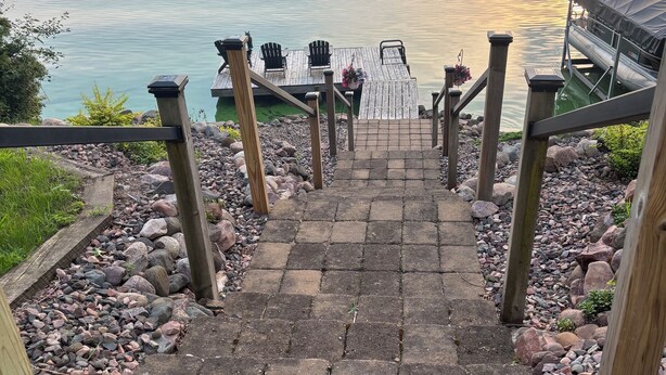 Un escalier en bois mène à une jetée où se trouvent des chaises et une table, le tout étant entouré de rochers et de verdure.
