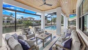 A spacious outdoor patio with a pool, comfortable seating, and a ceiling fan. - Exquisite Waterfront Home | Featuring Pool/Hot Tub (Marco Island)