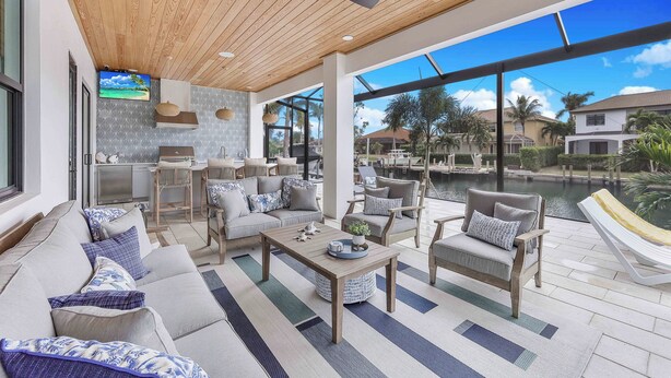 A spacious outdoor living area with a wooden ceiling, comfortable seating, a dining area, and a view of a body of water. - Exquisite Waterfront Home | Featuring Pool/Hot Tub (Marco Island)