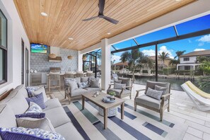 A spacious outdoor living area with a wooden ceiling, comfortable seating, a dining area, and a view of a body of water. - Exquisite Waterfront Home | Featuring Pool/Hot Tub (Marco Island)