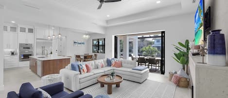 A modern open-plan living and dining area with a kitchen, large windows, and a ceiling fan.