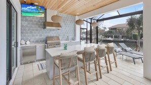 A modern kitchen with a large island, bar stools, and a view of a water body. - Exquisite Waterfront Home | Featuring Pool/Hot Tub (Marco Island)
