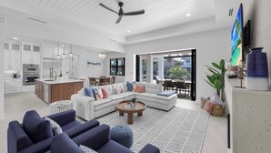 A modern open-plan living and dining area with a kitchen, large windows, and a ceiling fan. - Exquisite Waterfront Home | Featuring Pool/Hot Tub (Marco Island)