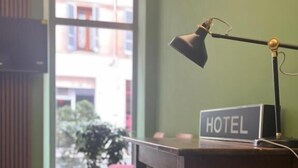 A hotel room with a wooden desk, a lamp, a sign reading "HOTEL", and a view of the outside through a window. - HOTEL BRENTA  (Parma)