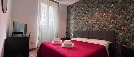 A hotel room with a bed, a desk, a chair, a television, and a window with curtains.