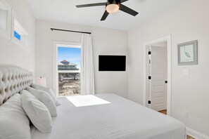 A bedroom with a large bed, a ceiling fan, a TV mounted on the wall, and a view of the outside. - Fort Morgan | Gulf and Bay Views | Beach Access (Gulf Shores)