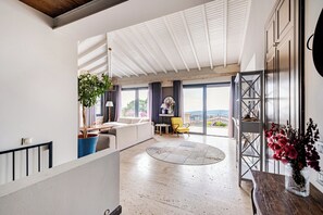 A spacious living area with a high ceiling, a round rug, a sofa, a yellow chair, and a view through large windows. - Luxury Villa Sunset Cesme with sea view and private pool in Çeşme (Çesme)