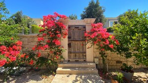 Una entrada de piedra con una puerta de madera, rodeada de vibrantes flores de buganvilla rosa.