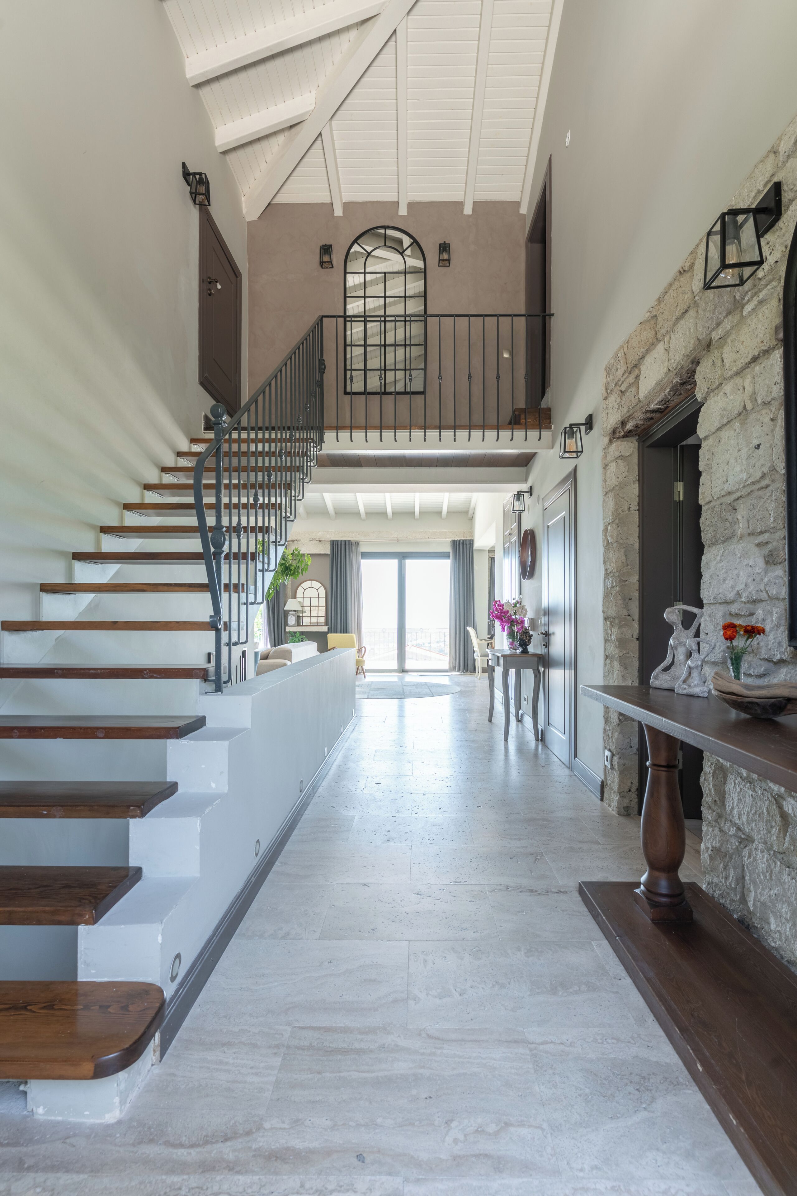Un interior espacioso con una escalera que lleva a una zona superior, una chimenea de piedra y vistas al exterior.