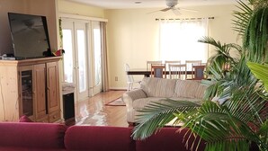 A living room with a red sofa, wooden flooring, a ceiling fan, and a dining area with a table and chairs.